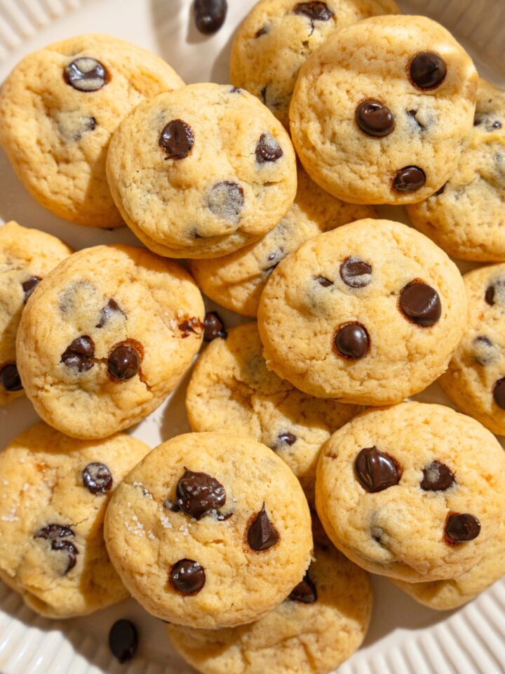 A bunch of mini chocolate chip cookies stacked on top of one another on a white plate.
