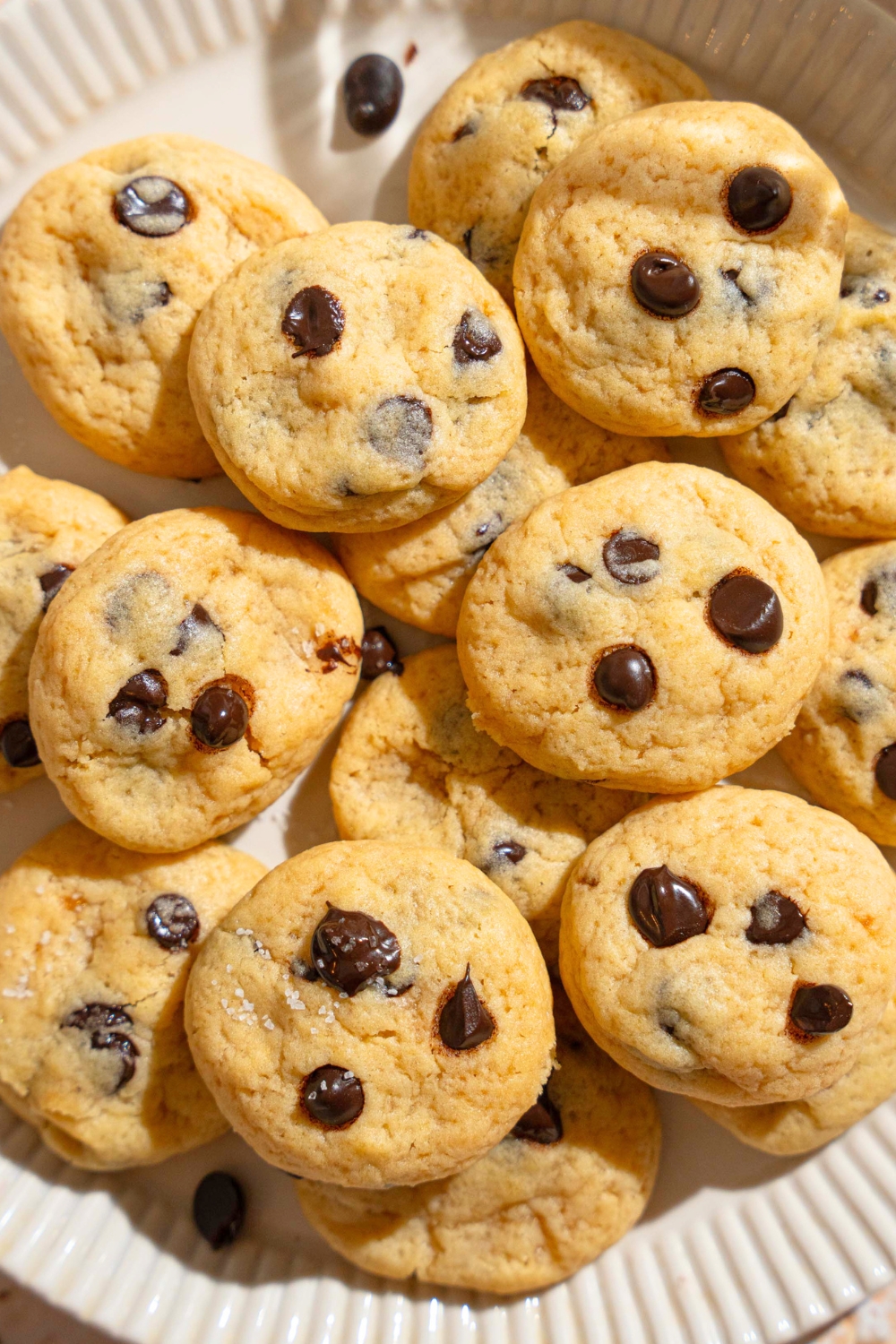 A bunch of mini chocolate chip cookies stacked on top of one another on a white plate.