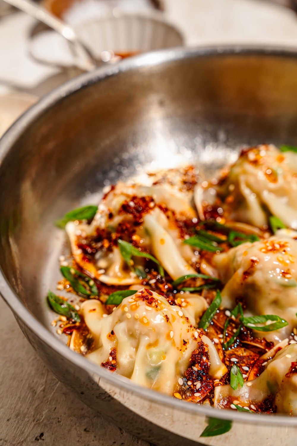 A skillet with pan fried pork and shrimp dumplings topped with sliced green onion, sesame seeds, and a soy sauce chili oil mixture. The skillet is on a tan counter.