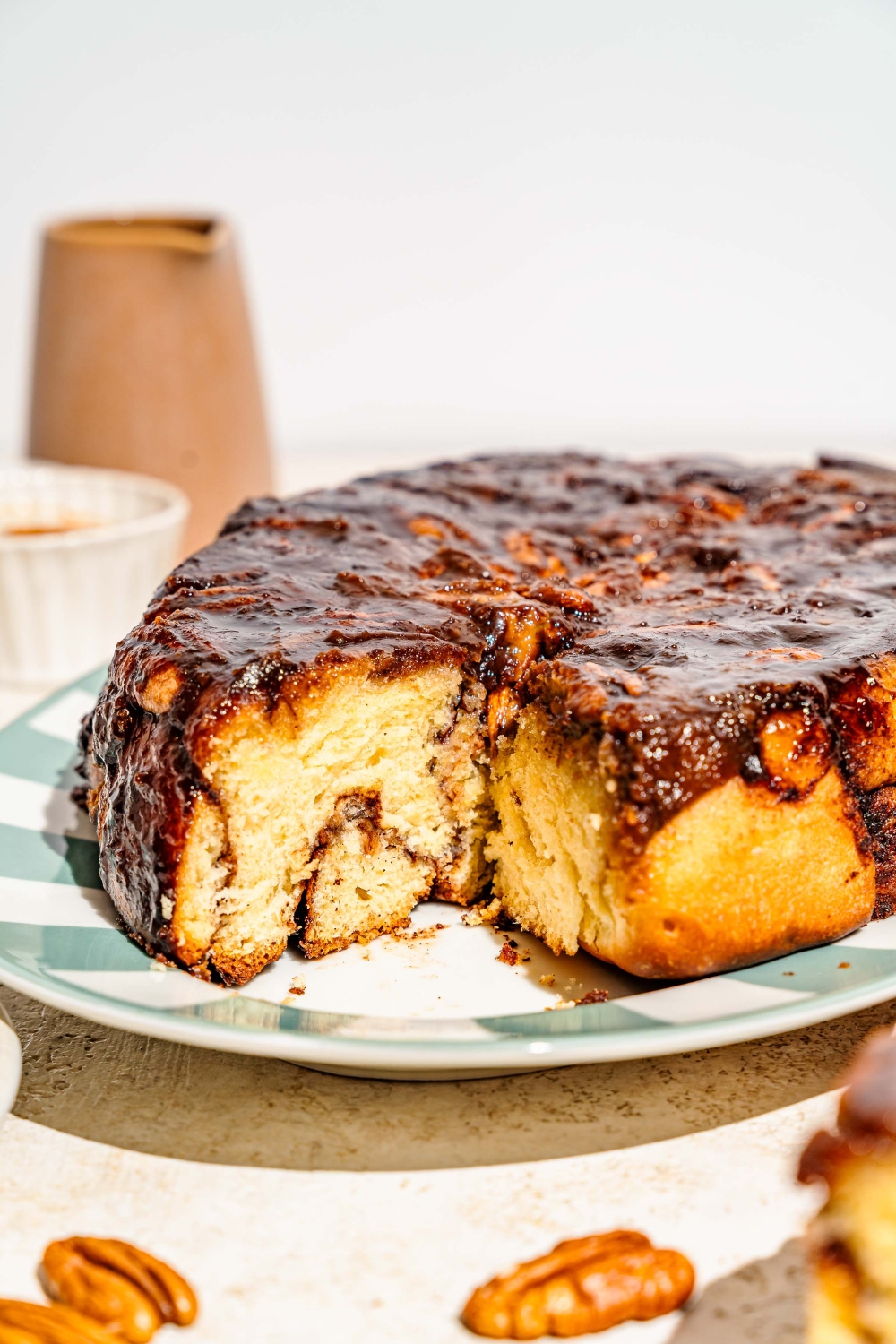 An oval tray with pecan caramel sticky buns. A bun has been removed from the tray. The tray is on a tan counter.