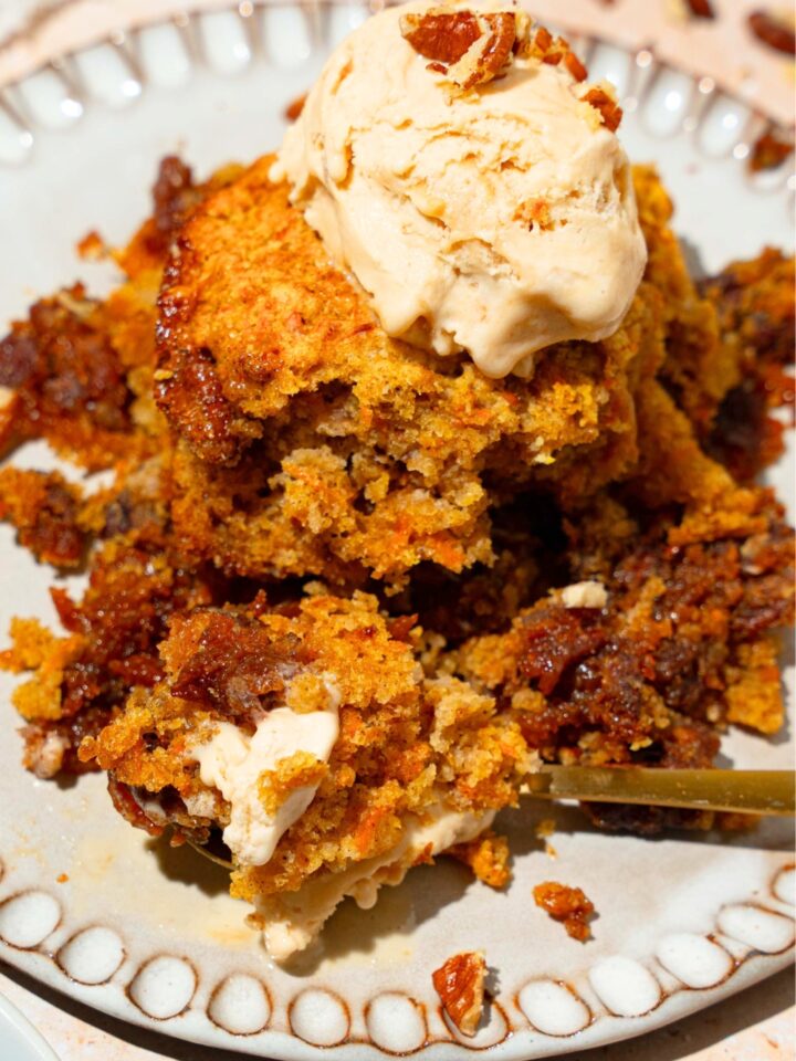 A scoop of pecan pie carrot cake cobbler with vanilla ice cream on top on a white plate.