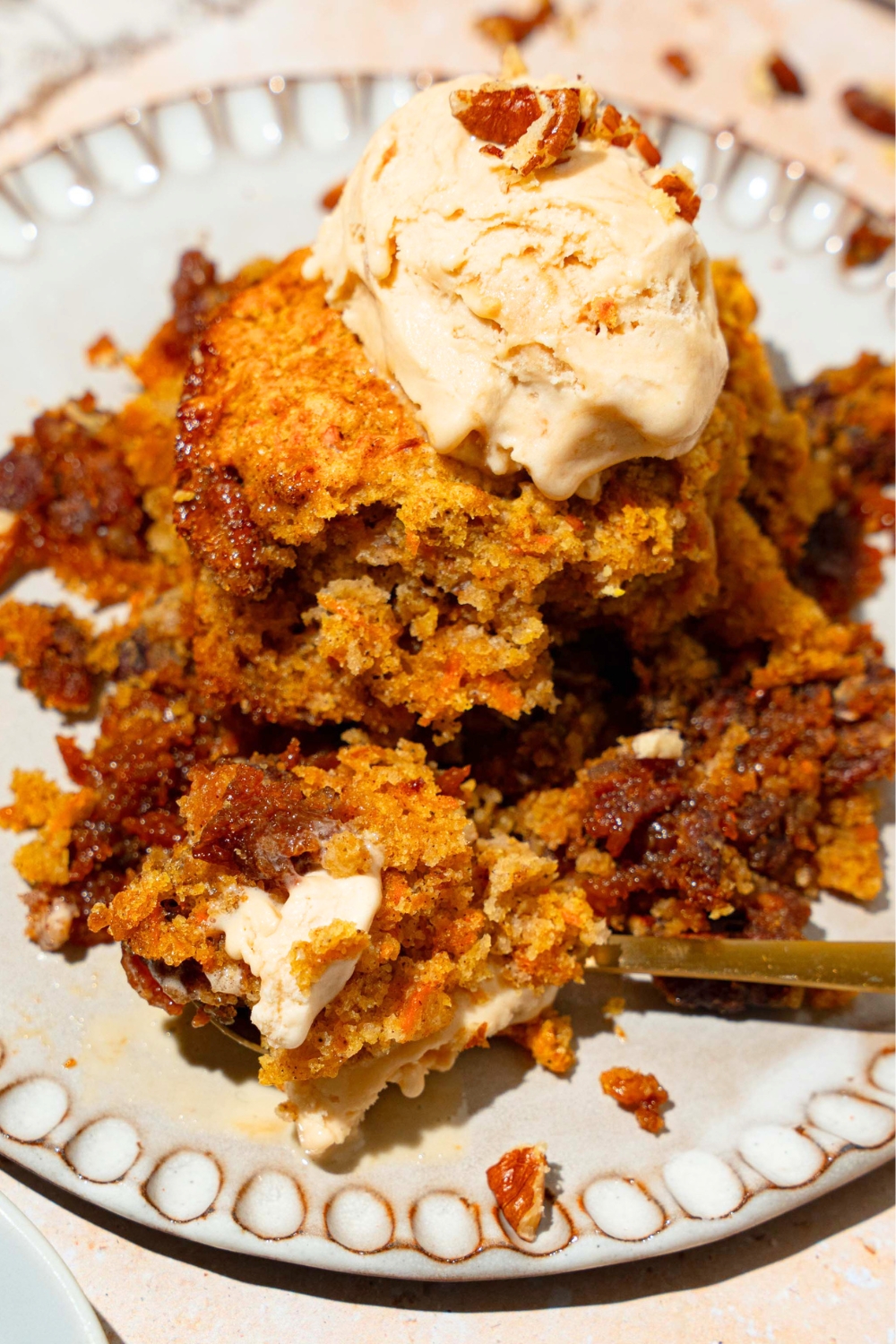 A scoop of pecan pie carrot cake cobbler with vanilla ice cream on top on a white plate.
