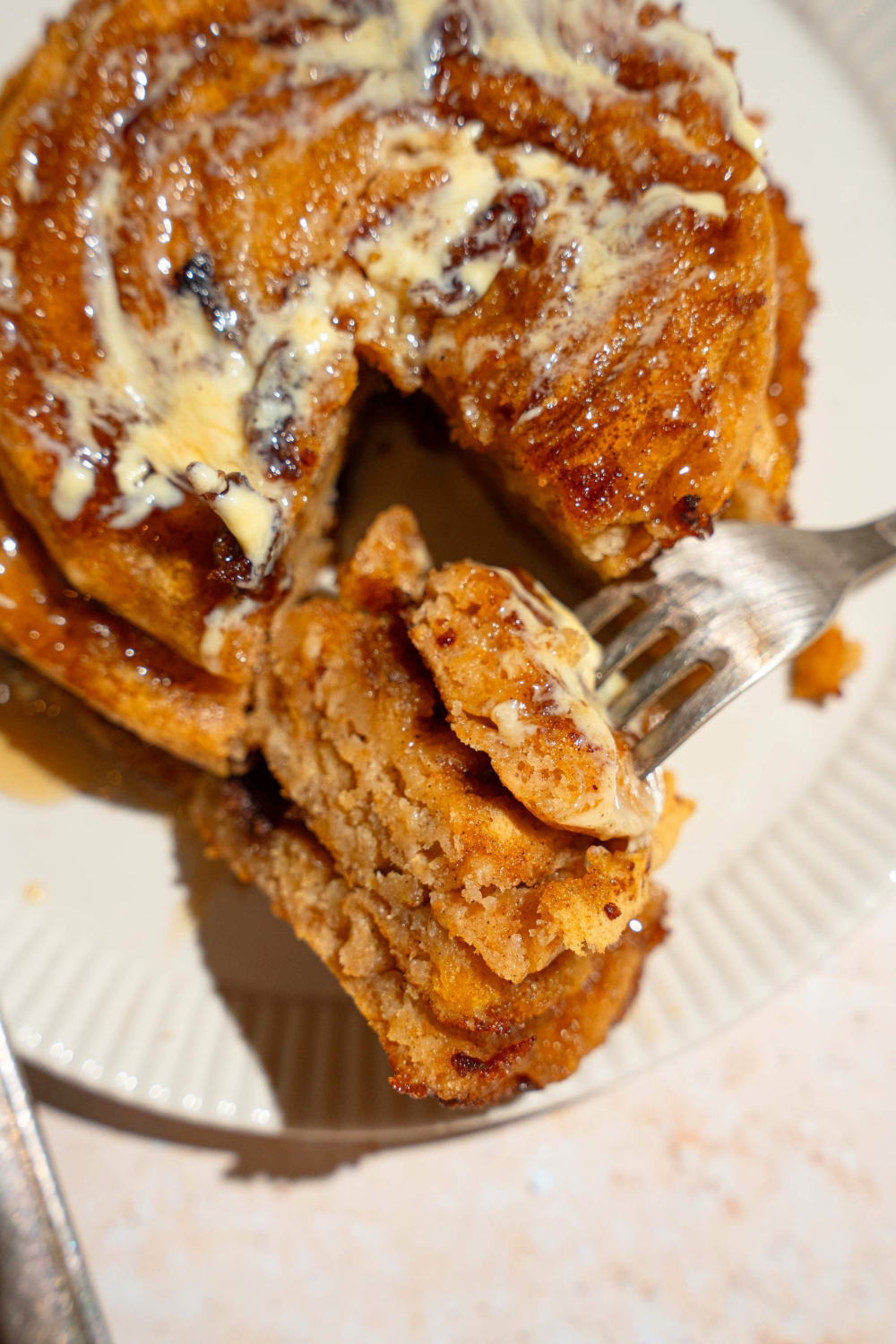 A fork with three pieces of pumpkin pancakes on it in front of the stack of pumpkin pancakes.