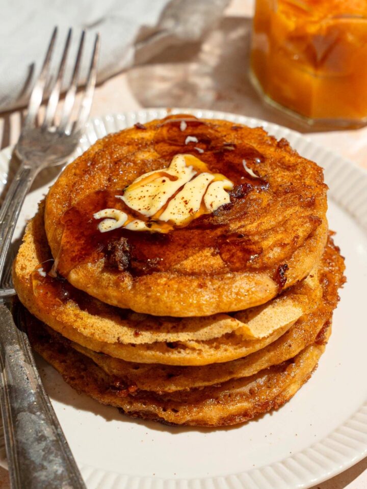 A stack of pumpkin pancakes with pancake mix that has butter and maple syrup on top on a white plate.