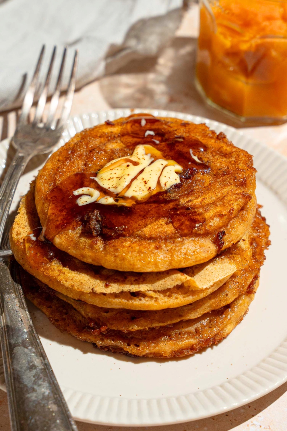 A stack of pumpkin pancakes with pancake mix that has butter and maple syrup on top on a white plate.