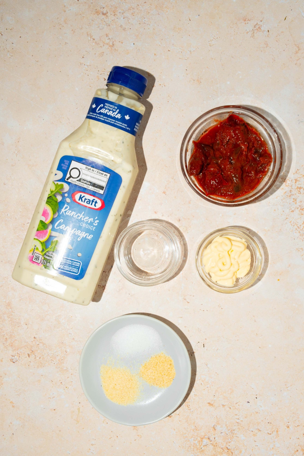 A bottle of ranch dressing, a glass bowl filled with chipotle, peppers, and adobo, a small glass bowl of vinegar, small glass bowl of mayo, and small plate with salt, garlic powder, and onion powder.