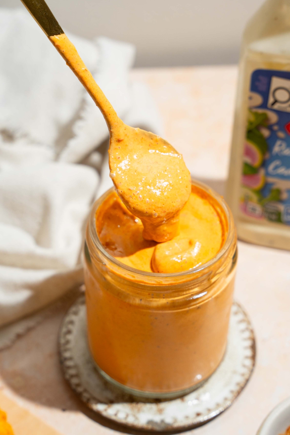 A spoon with southwest chipotle sauce on it drizzling some of the sauce into a glass jar that is filled with the southwest chipotle sauce.