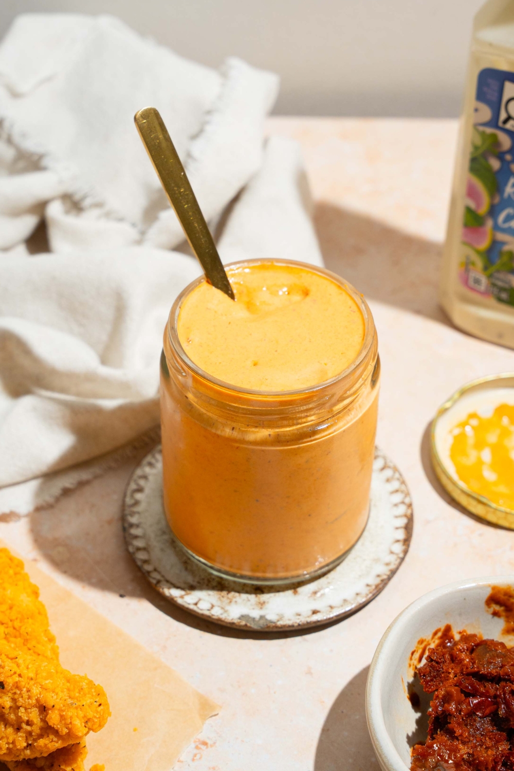A glass jar that is filled with southwest chipotle sauce on a small white plate on a white counter.
