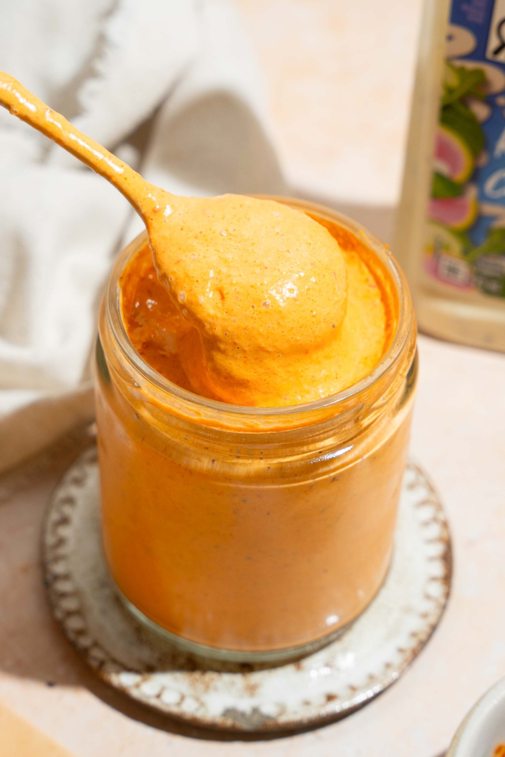 A spoon that has southwest chipotle sauce on it being held directly above a glass jar that is filled with the southwest chipotle sauce.