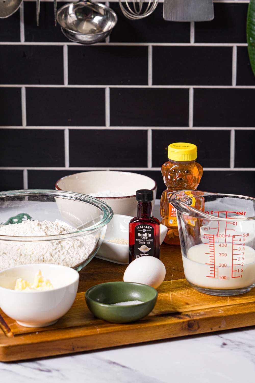 A wooden board with ingredients to make tiana's beignets including flour, milk, egg, butter, yeast, sugar, powdered sugar, and honey.
