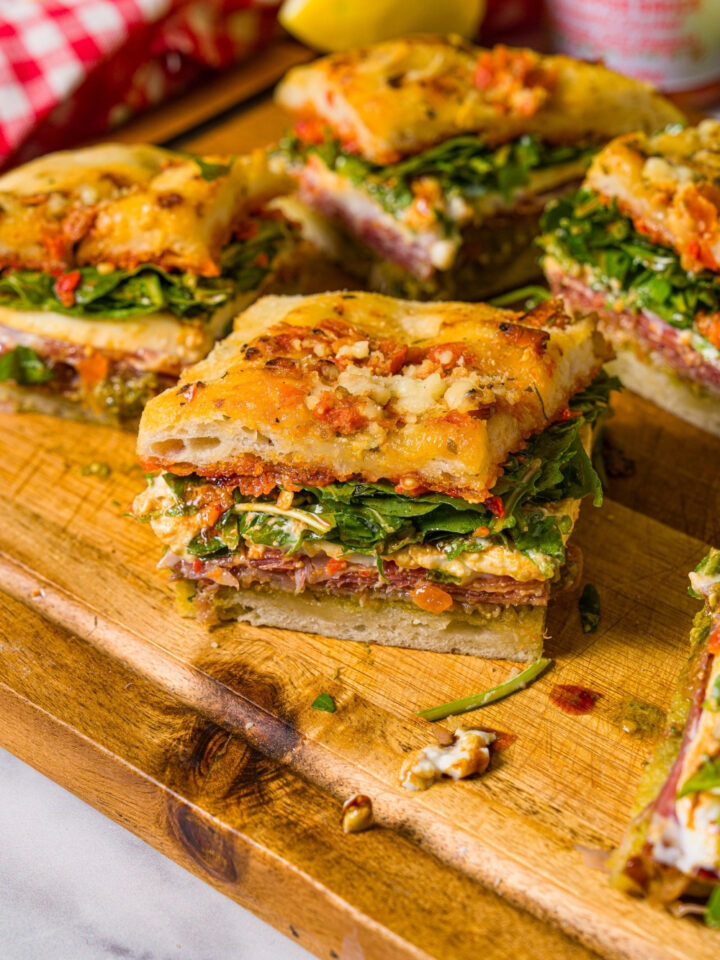 A square of Trader Joe's focaccia sandwich on a wooden cutting board with more squares of the sandwich behind it.