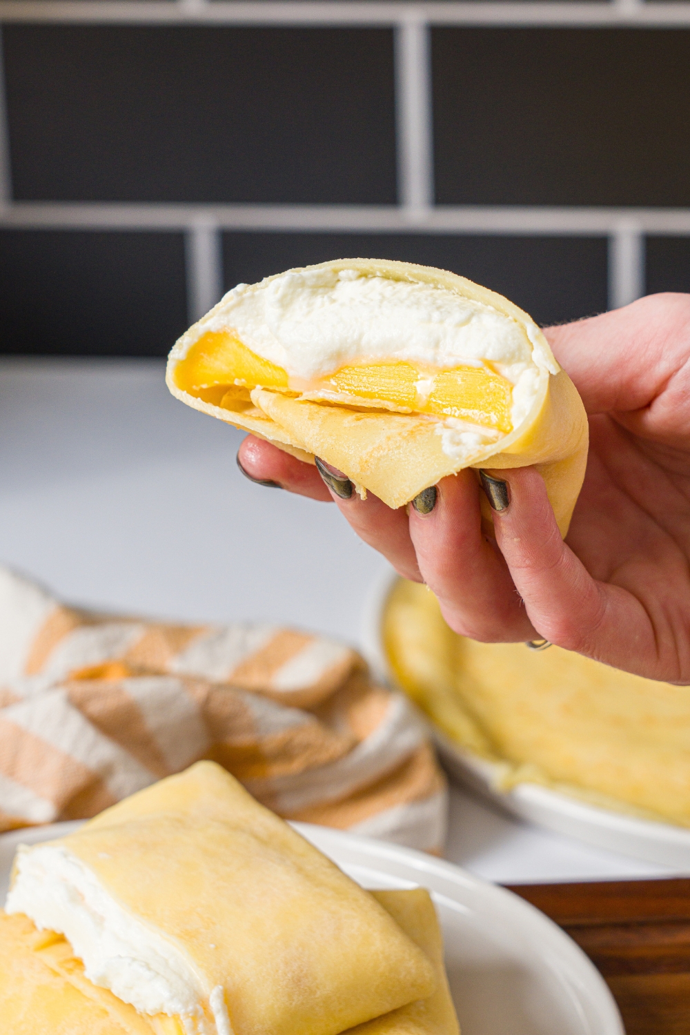 A hand holding a half of a mango pancake with the inside facing out.