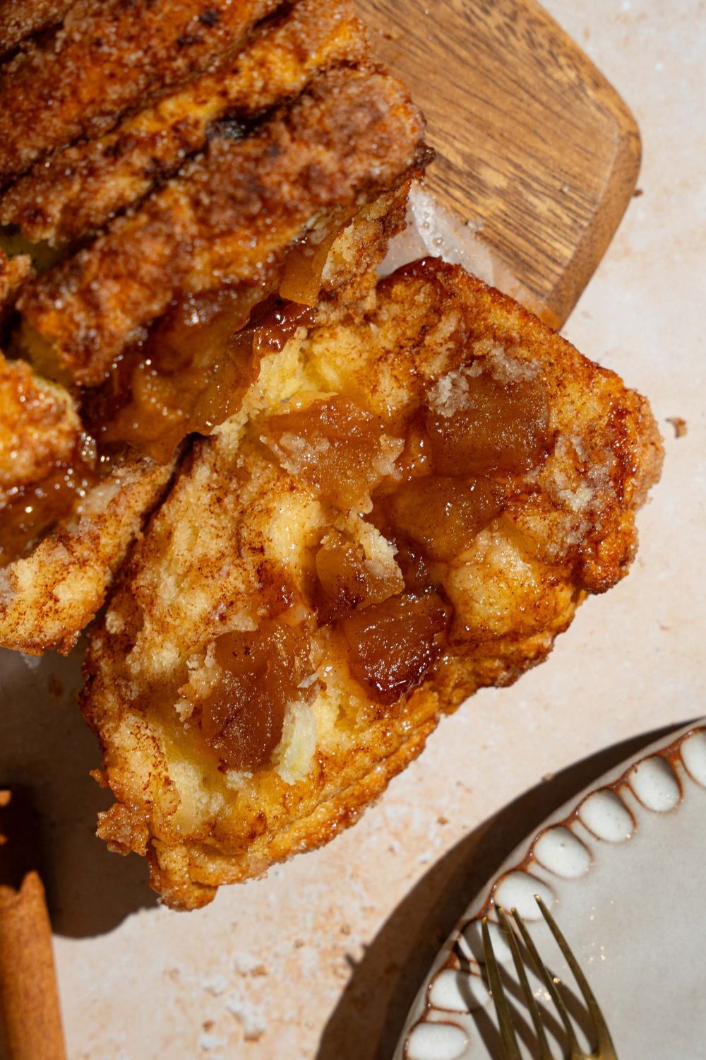 A loaf of apple pie pull apart bread on a wooden board on a tan counter. One slice of the loaf is tipped over.