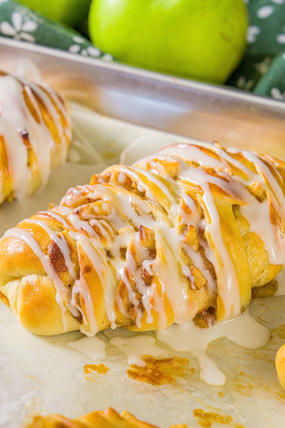 A baking sheet lined with parchment paper with twisted apple pie rolls drizzled with icing.