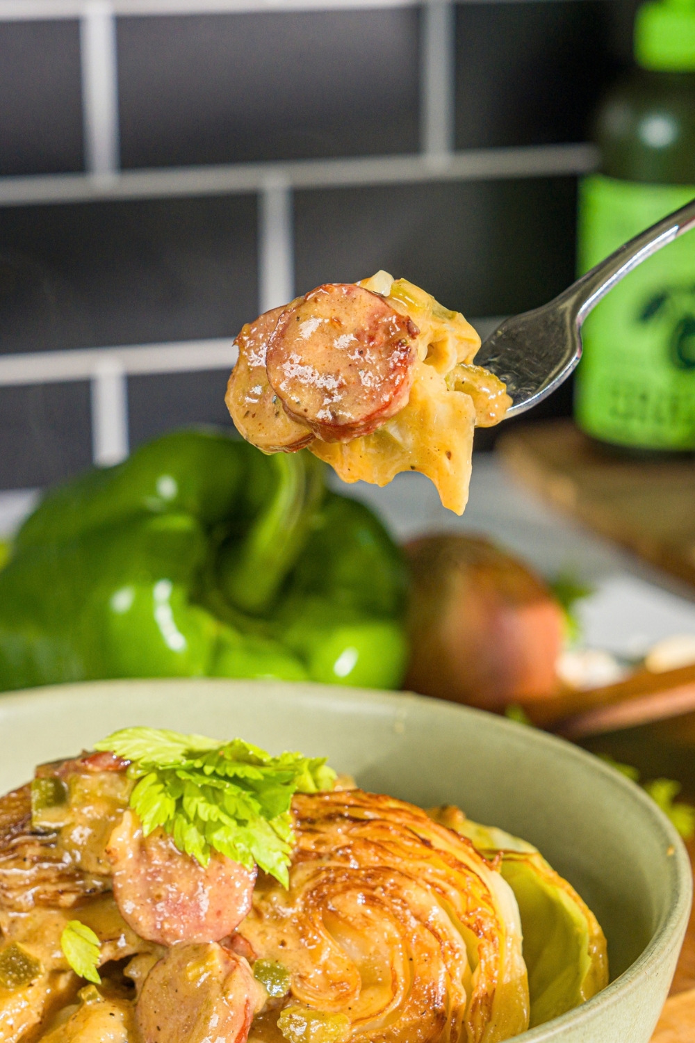 A bowl with southern smothered cabbage with sausage garnished with fresh parsley. A fork is taking a bite from the bowl.