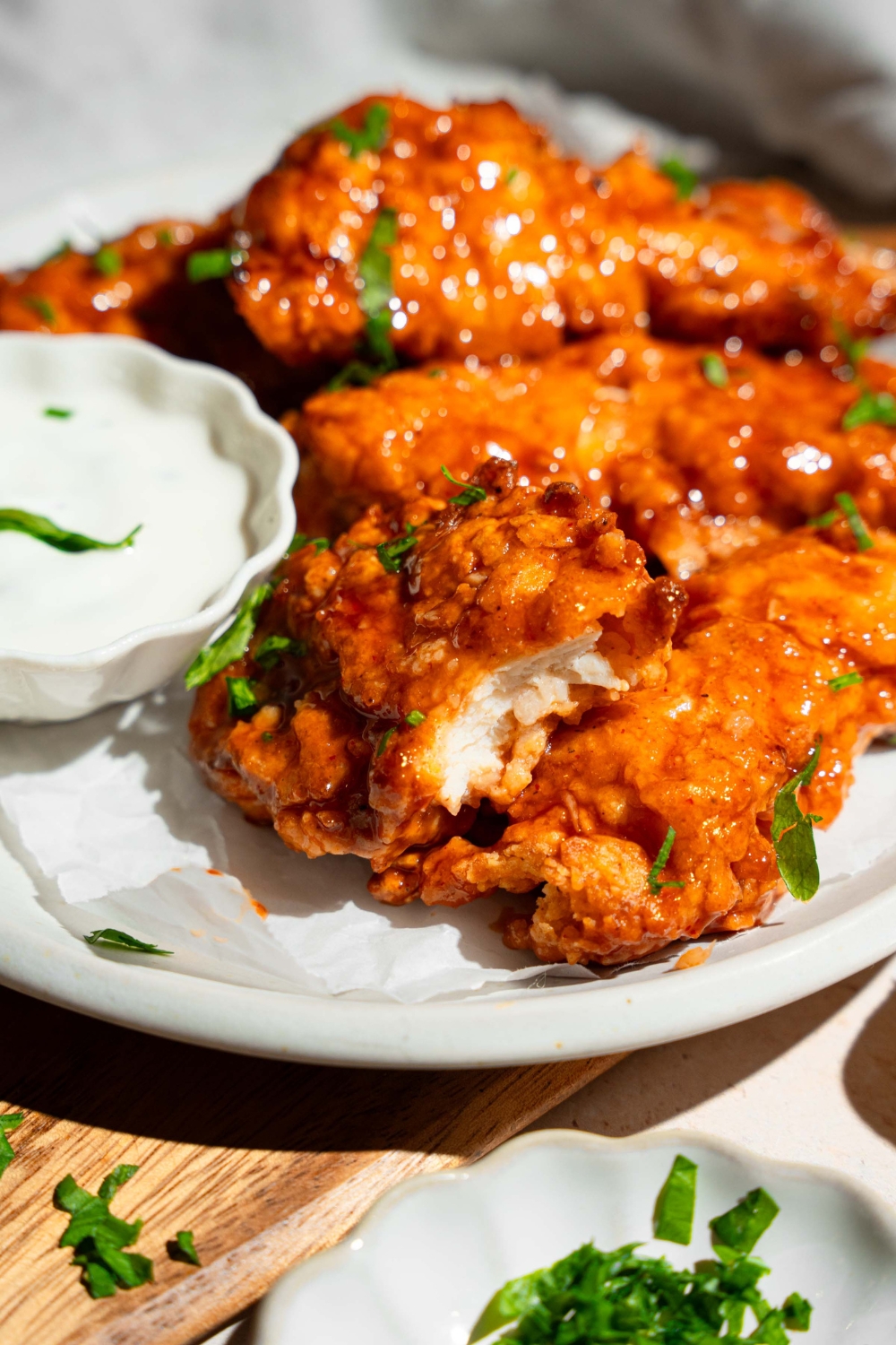 A white plate with sweet chili chicken tenders garnished with fresh parsley and served with a small bowl of dipping sauce. One of the tenders has a bite removed.
