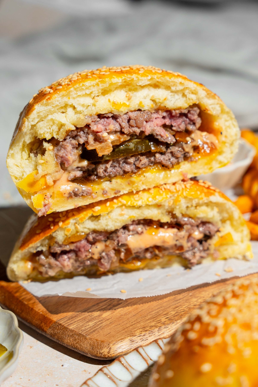 A wooden board lined with parchment paper with a burger stuffed bun sliced in half and stacked on top of each other.