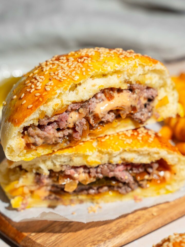 A wooden board lined with parchment paper with a burger stuffed bun sliced in half and stacked on top of each other.