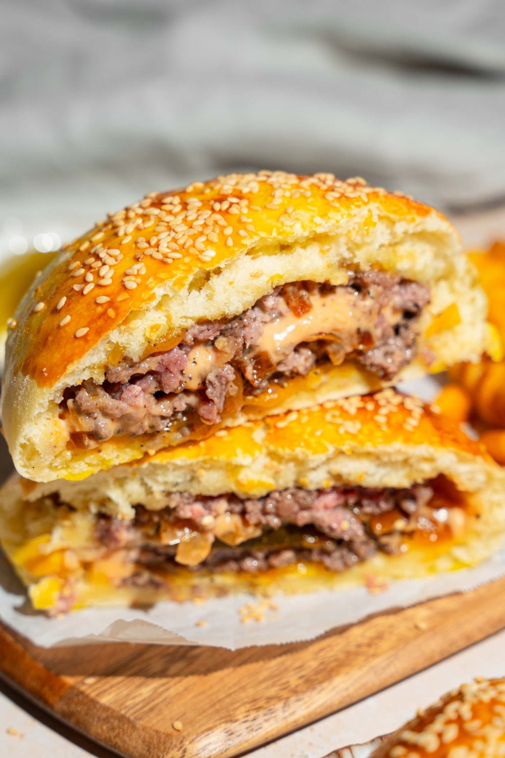 A wooden board lined with parchment paper with a burger stuffed bun sliced in half and stacked on top of each other.