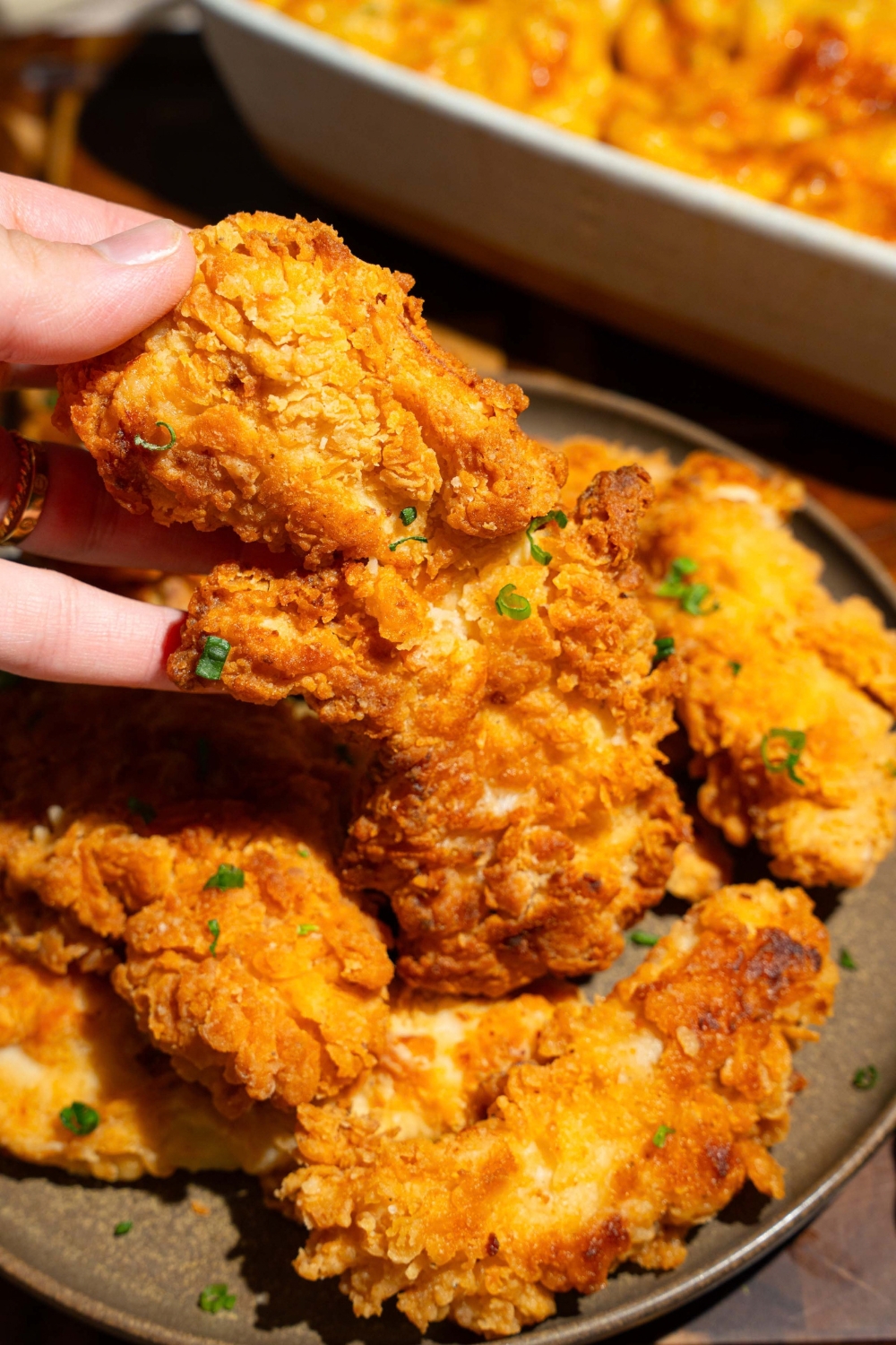 A plate of copycat Chick-Fil-A tenders garnished with fresh parsley. A hand is taking one of the tenders on a wooden board.
