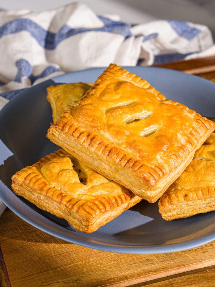 A blue plate with chicken pot pie hand pies. The plate is on a wooden board with a blue striped napkin.