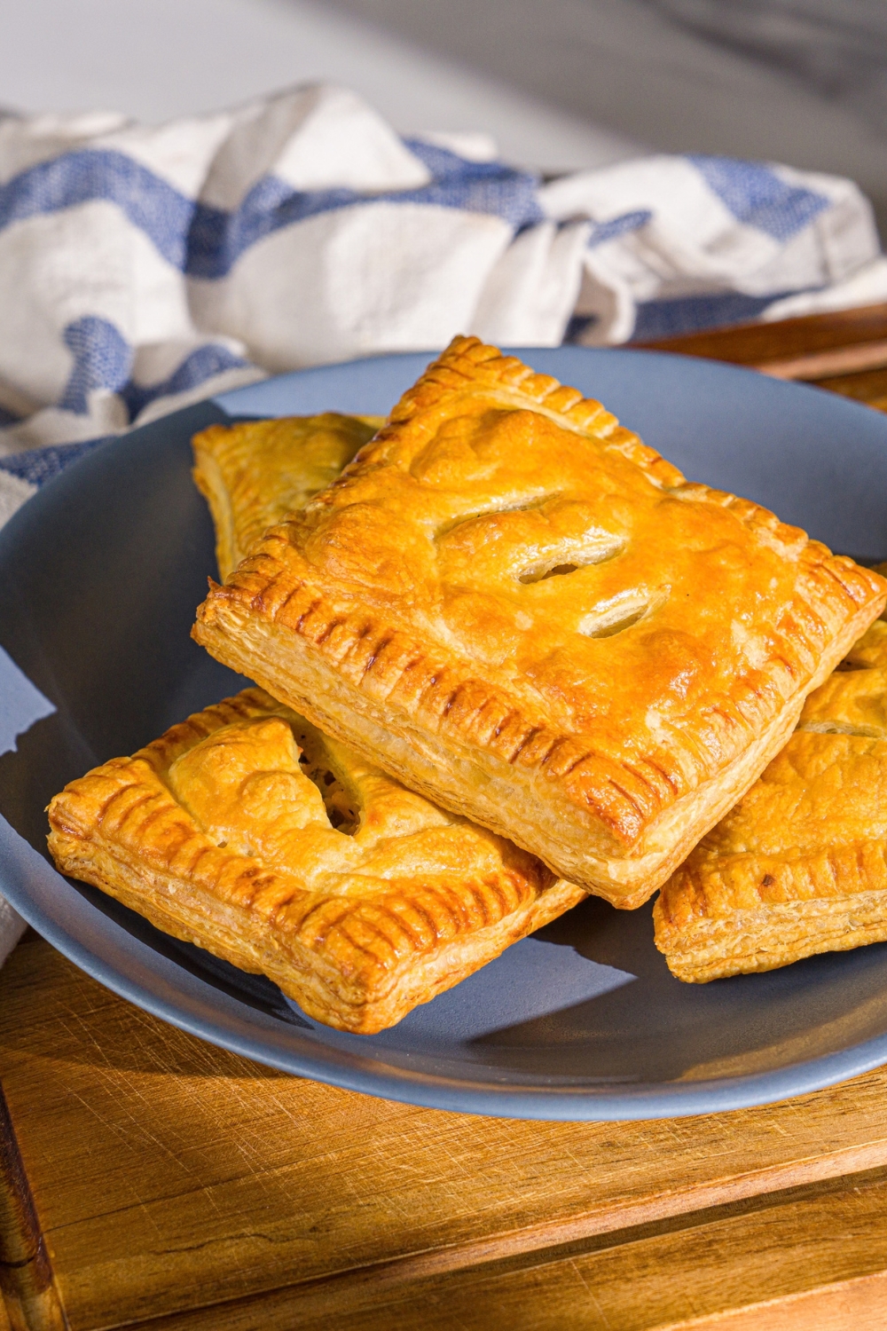 A blue plate with chicken pot pie hand pies. The plate is on a wooden board with a blue striped napkin.