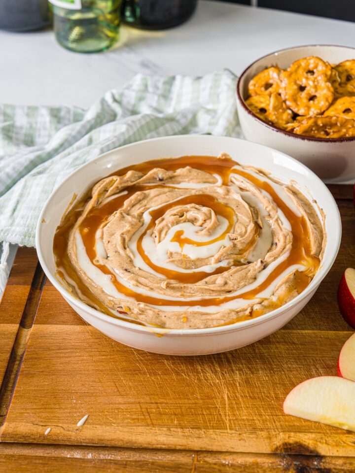 Cinnamon roll dip with icing and caramel sauce in a white bowl.