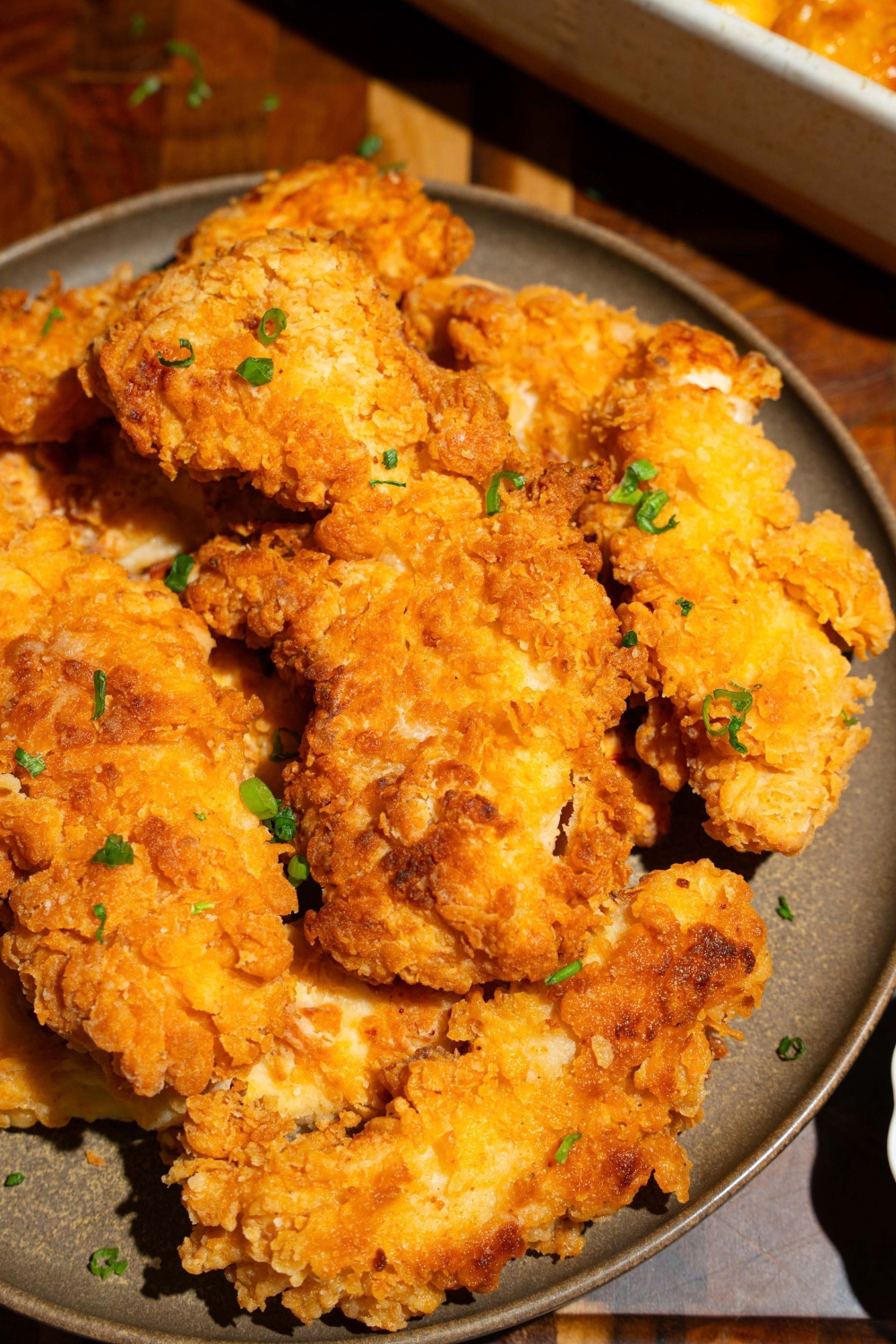 A green plate with copycat Chick-Fil-A tenders garnished with fresh parsley. The plate is on a wooden board.