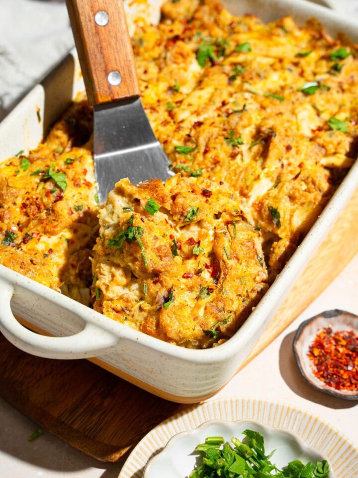 A baking dish with Dolly Parton's chicken and stuffing casserole garnished with fresh parsley. A spatula is taking a piece from the casserole.