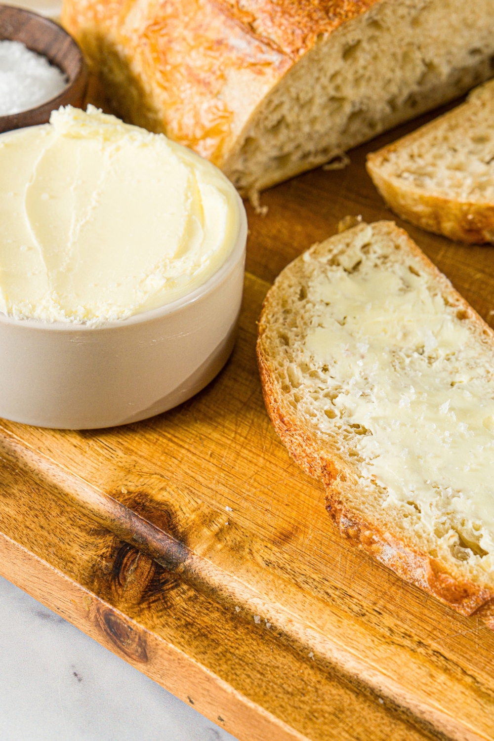 A wooden board with a small bowl of cultured butter and a slice of bread spread with butter.