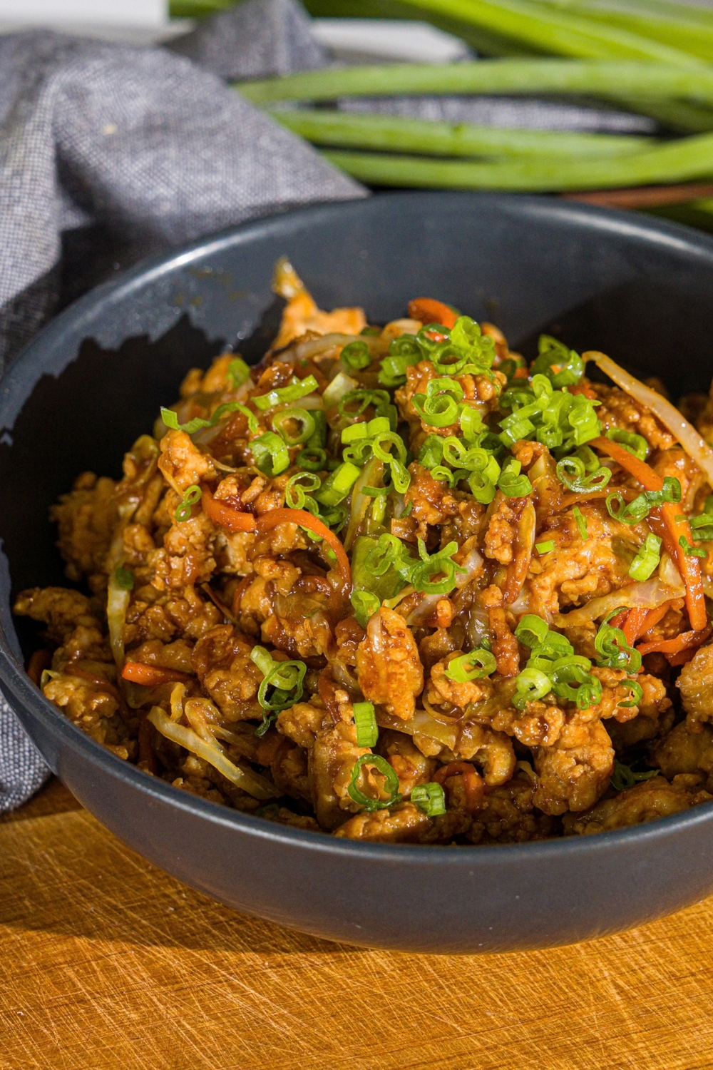 A navy bowl with an egg roll in a bowl, made with ground chicken and sautéed cabbage and carrots tossed in an egg roll sauce, all garnished with sliced green onions. The bowl is on a wooden board.