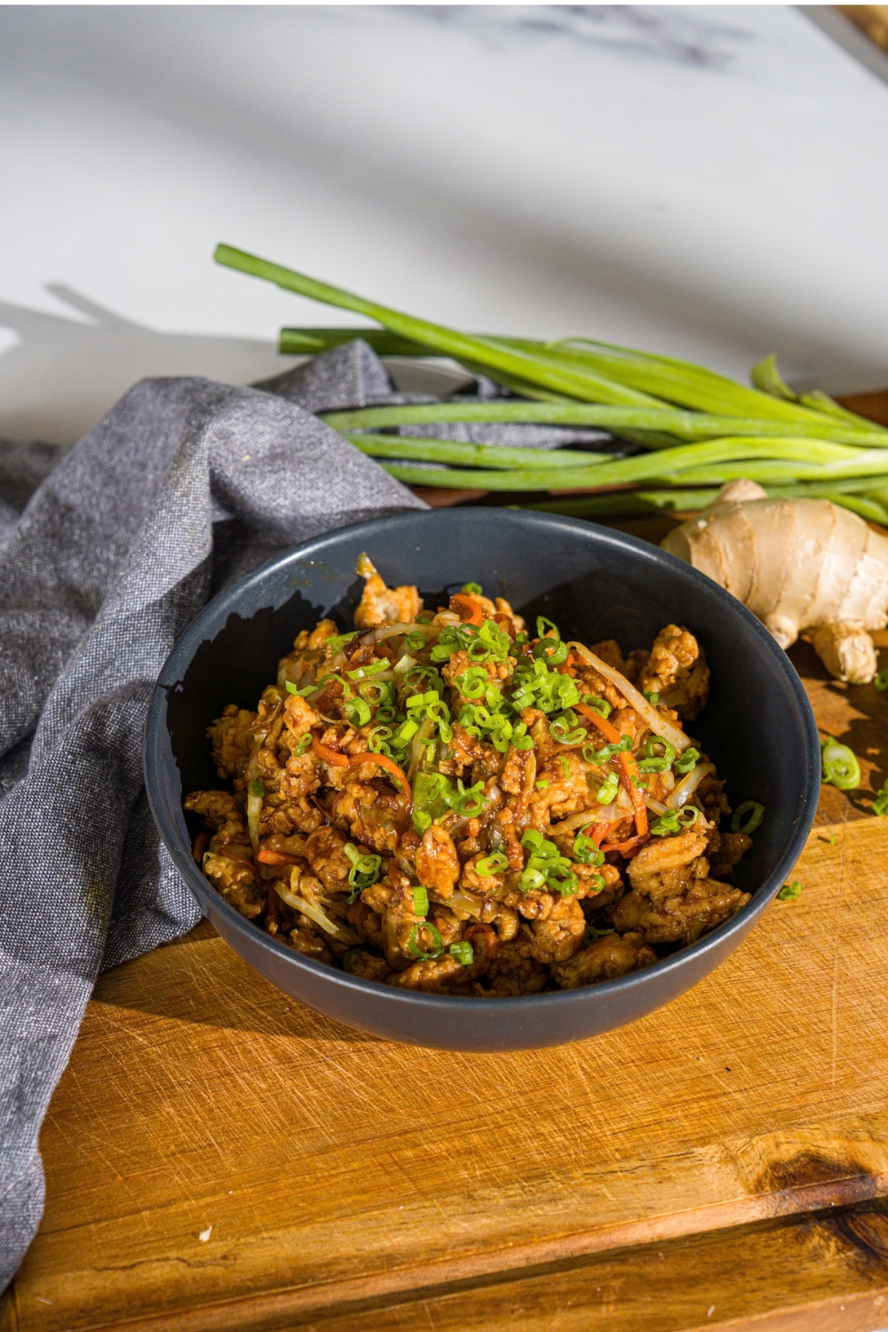A navy bowl with an egg roll in a bowl, made with ground chicken and sautéed cabbage and carrots tossed in an egg roll sauce, all garnished with sliced green onions. The bowl is on a wooden board with a blue cloth napkin.