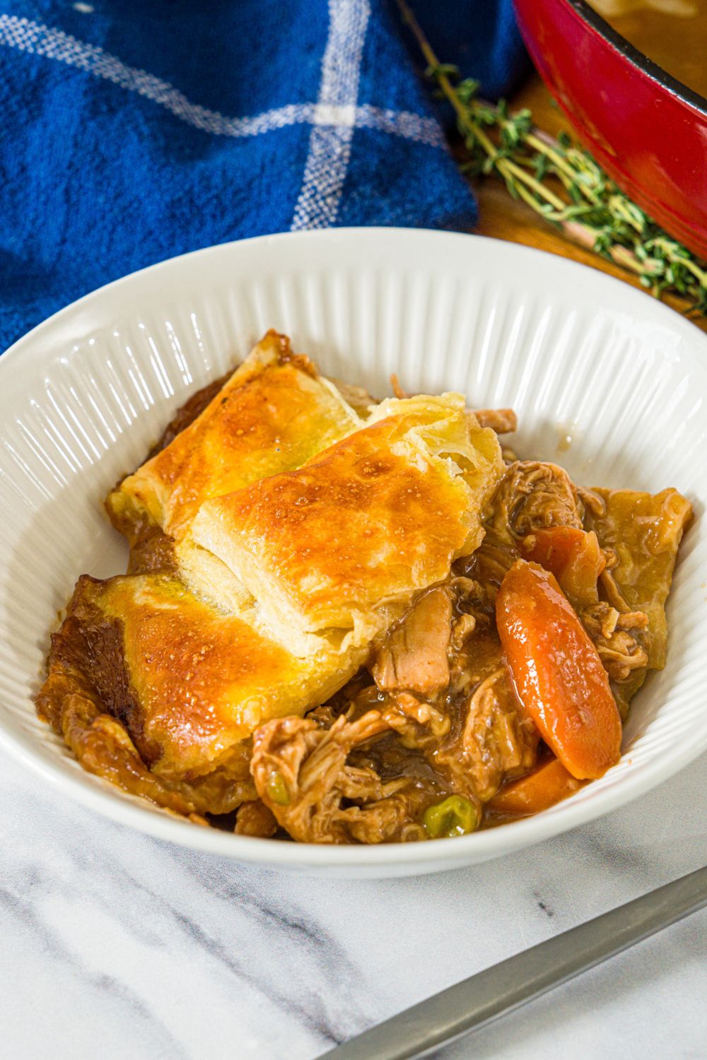 A white bowl with a slice of french onion chicken pot pie. The bowl is on a marble counter with a blue cloth napkin.