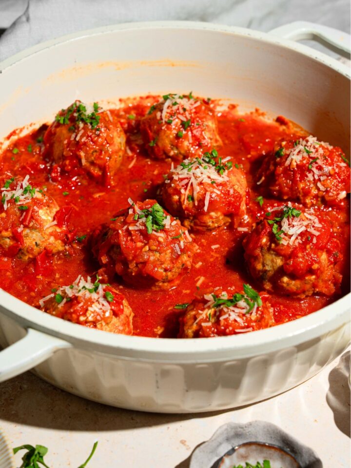 A bunch of hailey bieber chicken meatballs in tomato sauce in a white pot.