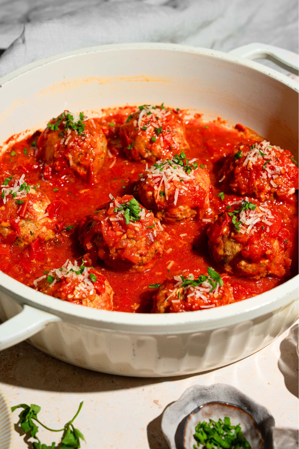 A bunch of hailey bieber chicken meatballs in tomato sauce in a white pot.