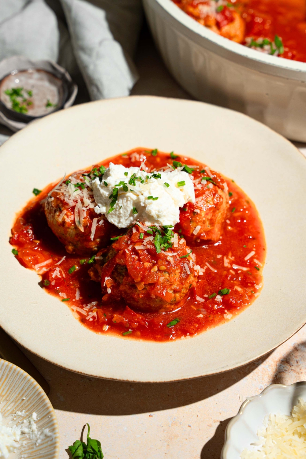 Cottage cheese on top of three chicken meatballs, and tomato sauce on a white plate.