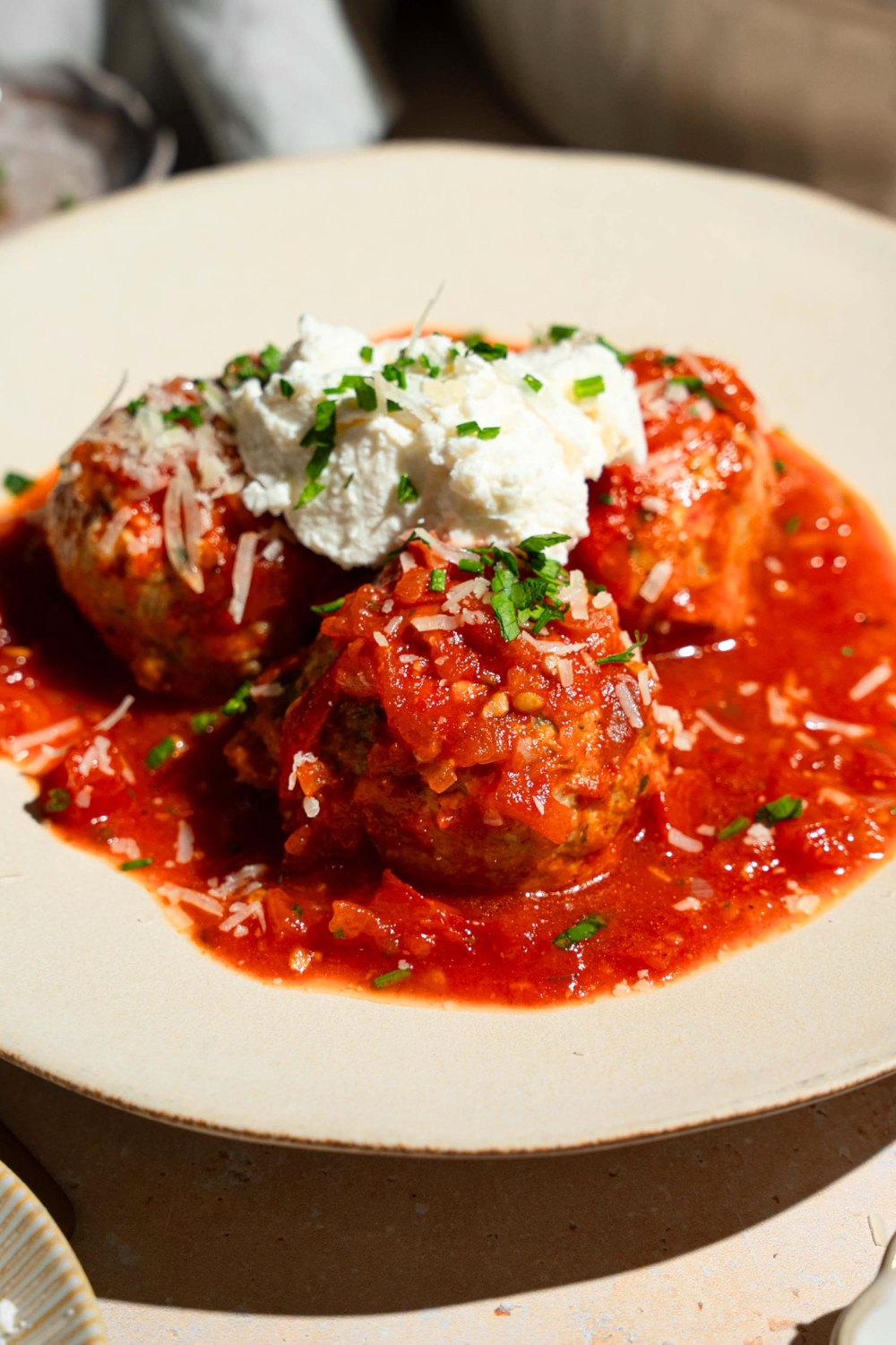 Three chicken meatballs with cottage cheese on top on tomato sauce on a white plate.