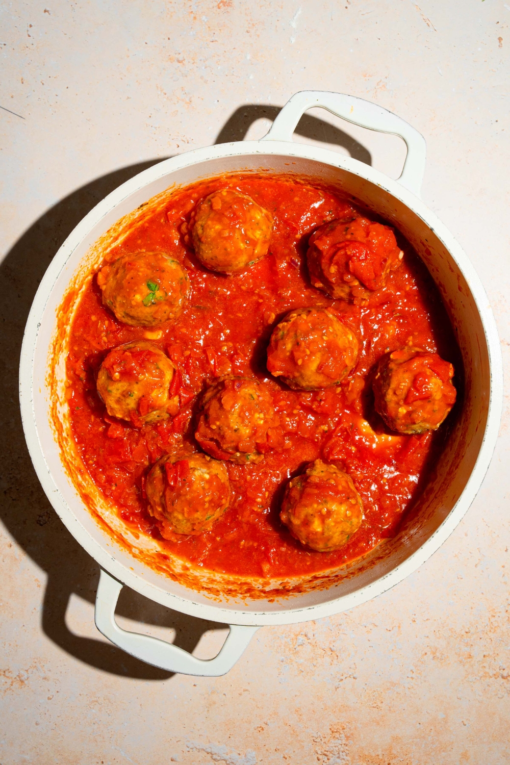 Nine chicken meatballs, cooking in a tomato sauce in a white pot.