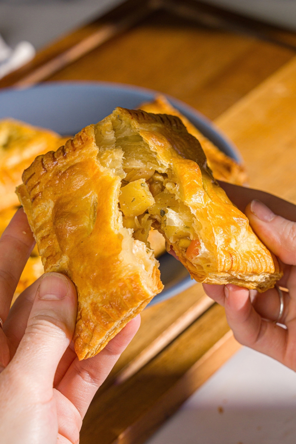 A close up of a hand pulling apart a chicken pot pie hand pie. There is a plate of hand pies blurred in the background.