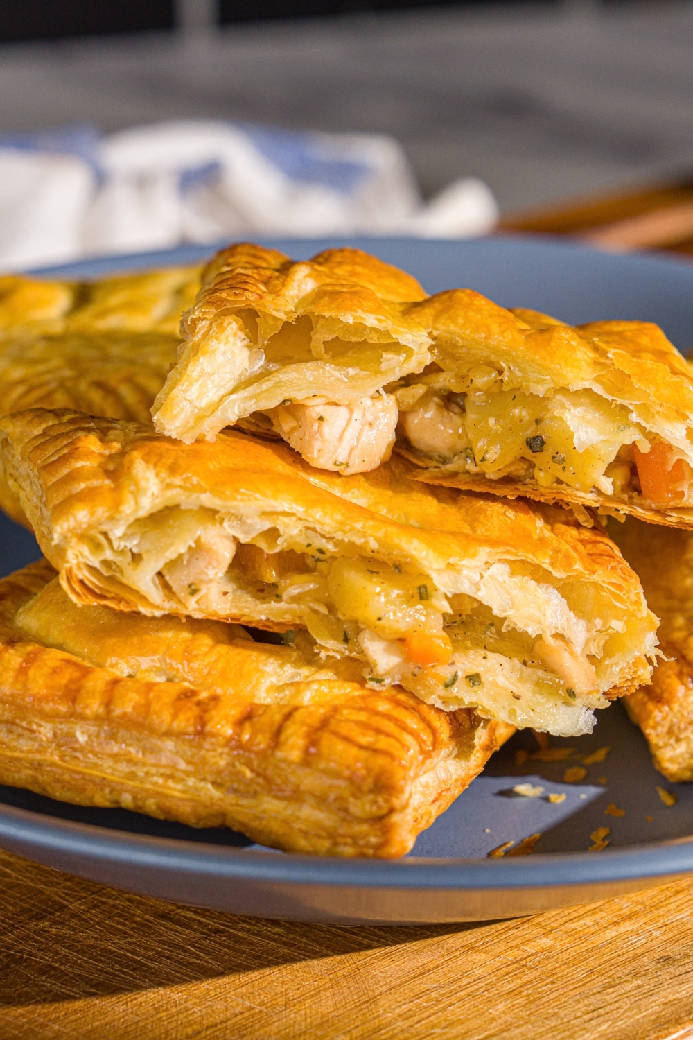 A blue plate with chicken pot pie hand pies. One of the pies is sliced in half. The plate is on a wooden board.