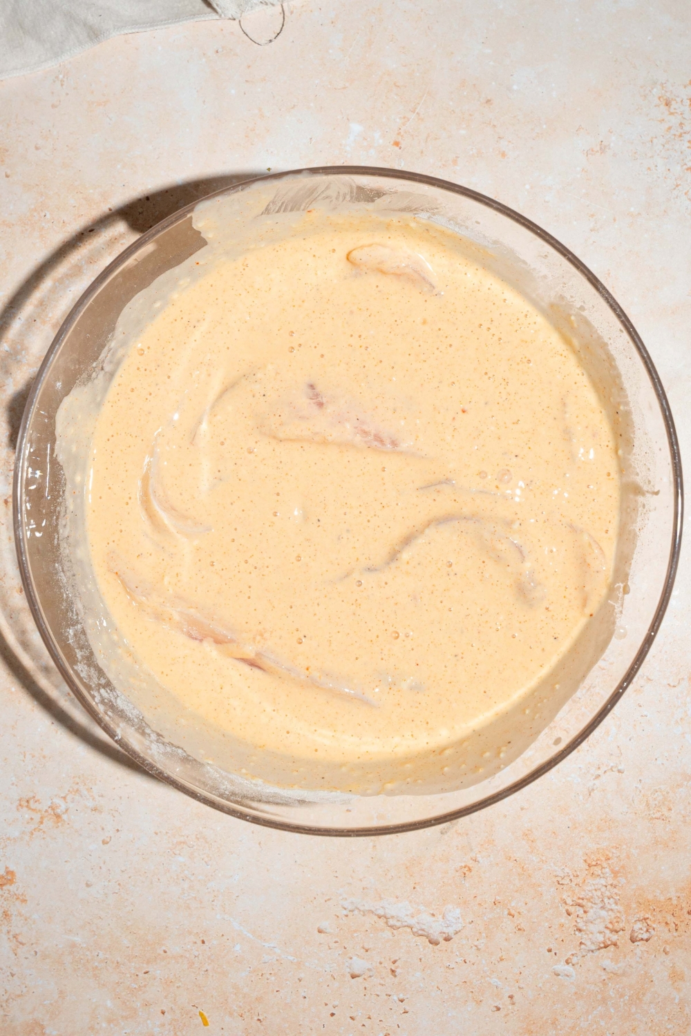 A large bowl with uncooked chicken tenders submerged in marinade. The bowl is on a tan counter.
