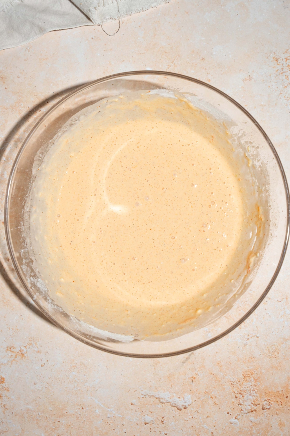 A large bowl with a chicken tender marinade including eggs, water, milk, and seasonings. The bowl is on a tan counter.