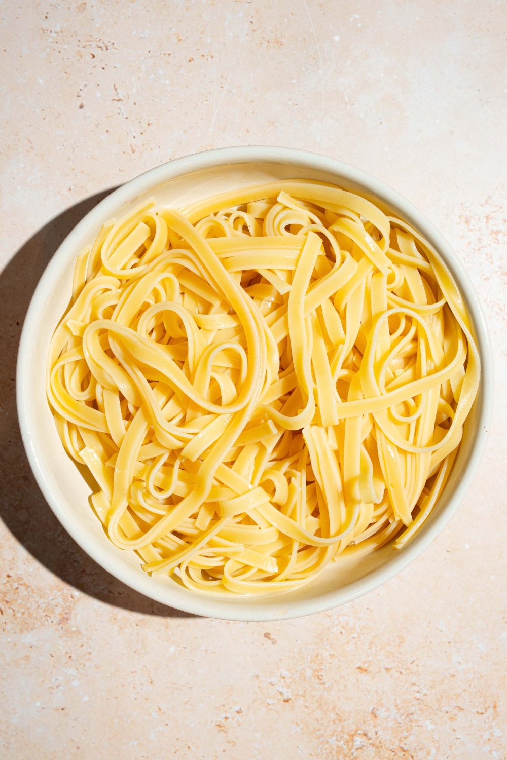 A bowl of fettuccine pasta. The bowl is on a tan counter.