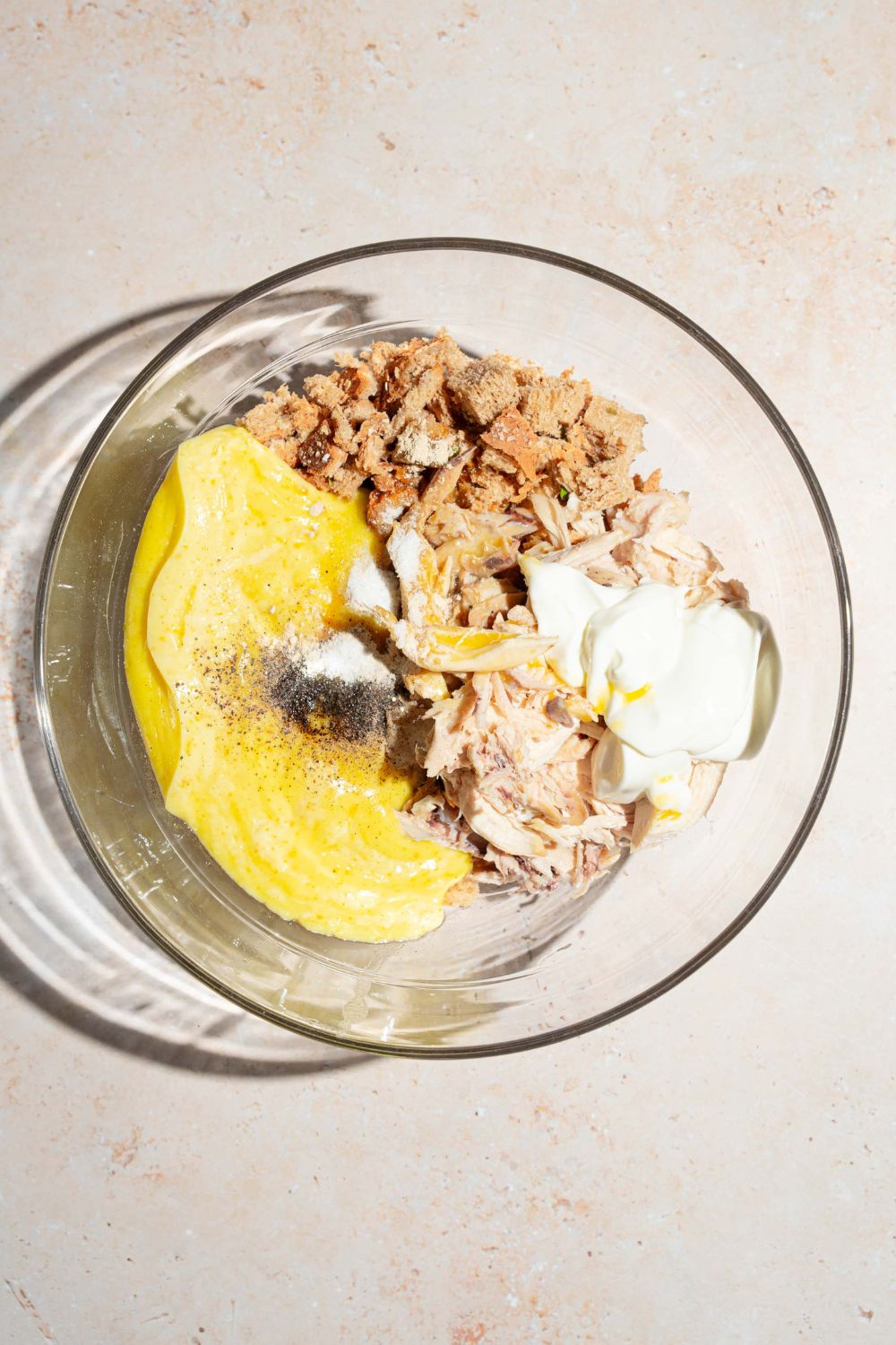 A large bowl with ingredients to make chicken and stuffing casserole including shredded chicken, cream of chicken soup, broth, butter, sour cream, and stuffing. The bowl is on a tan counter.