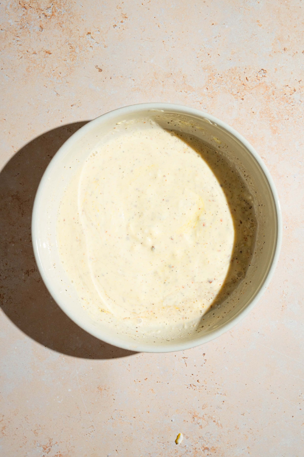 A large bowl with a creamy dressing for Japanese potato salad. The bowl is on a tan counter.