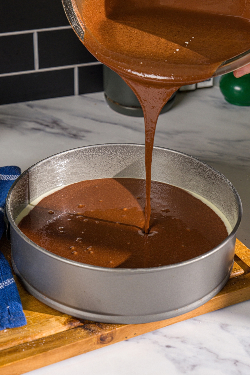 A bowl of Matilda cake batter being poured into a cake pan. The pan is on a wooden board.