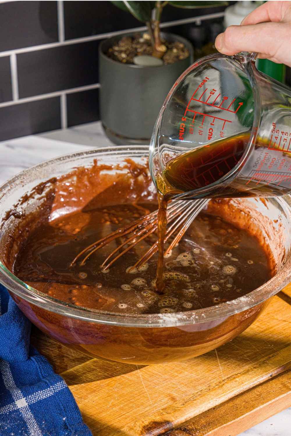 A large bowl with Matilda cake batter with a measuring cup adding coffee to the batter. The bowl is on a wooden board.