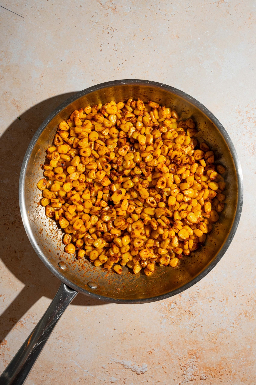 A skillet with cooked seasoned corn. The skillet is on a tan counter.