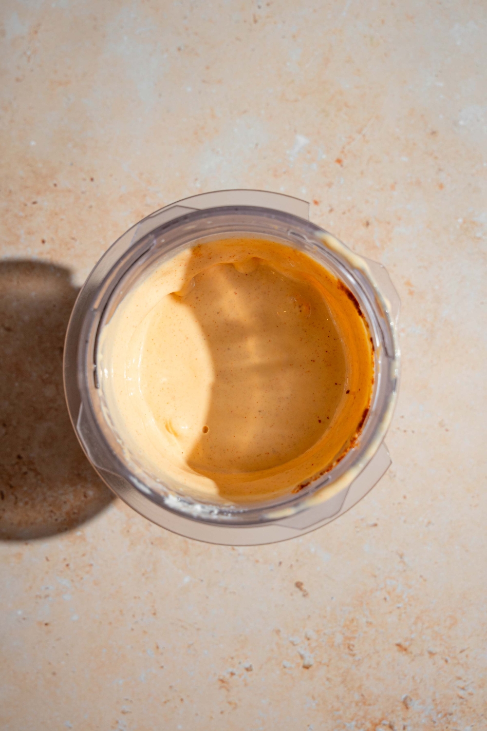 A blender jar with blended elote dressing with cottage cheese, cotija cheese, garlic, and lime. The jar is on a tan counter.