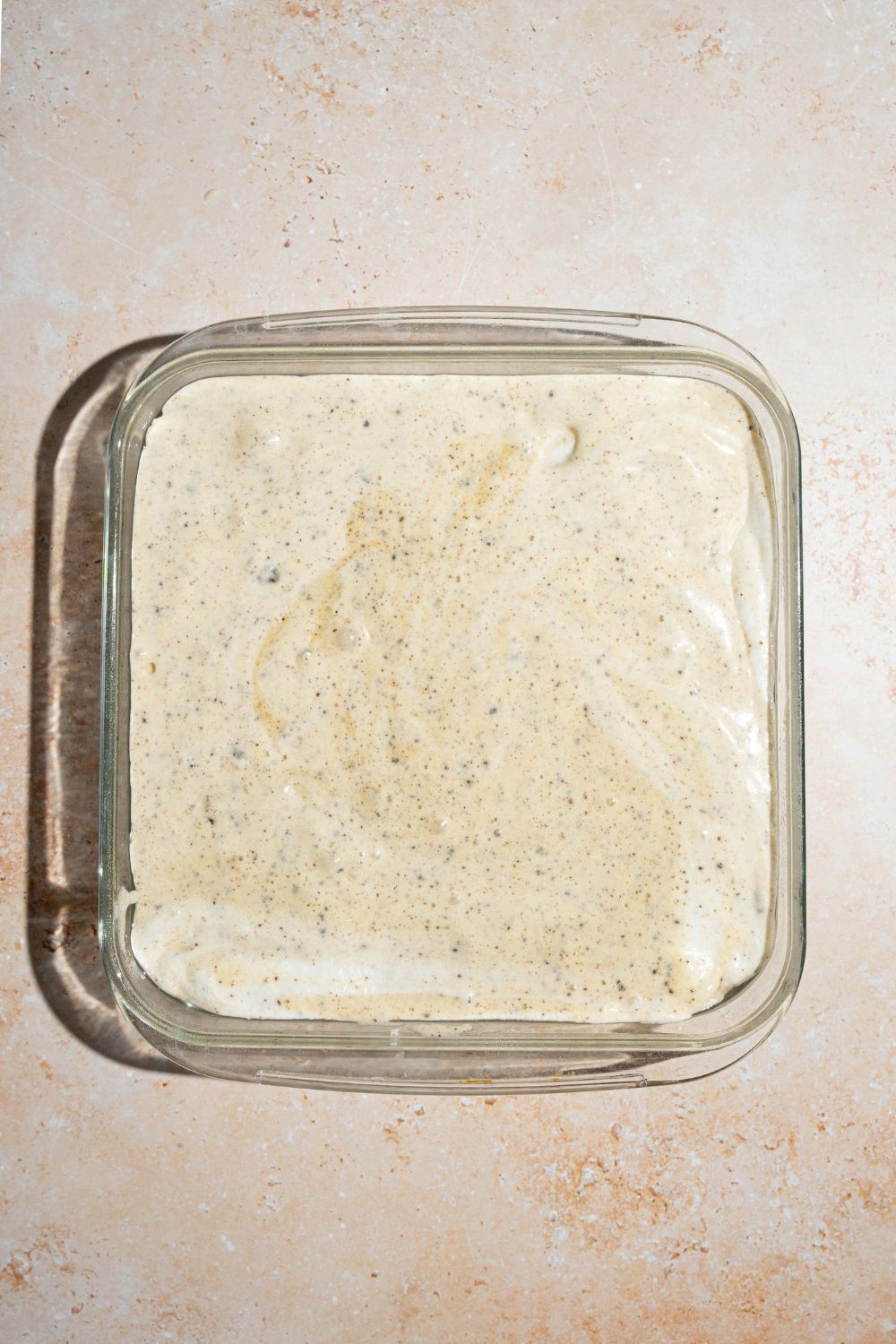 A square baking dish with Oreo tres leches cake batter. The dish is on a tan counter.